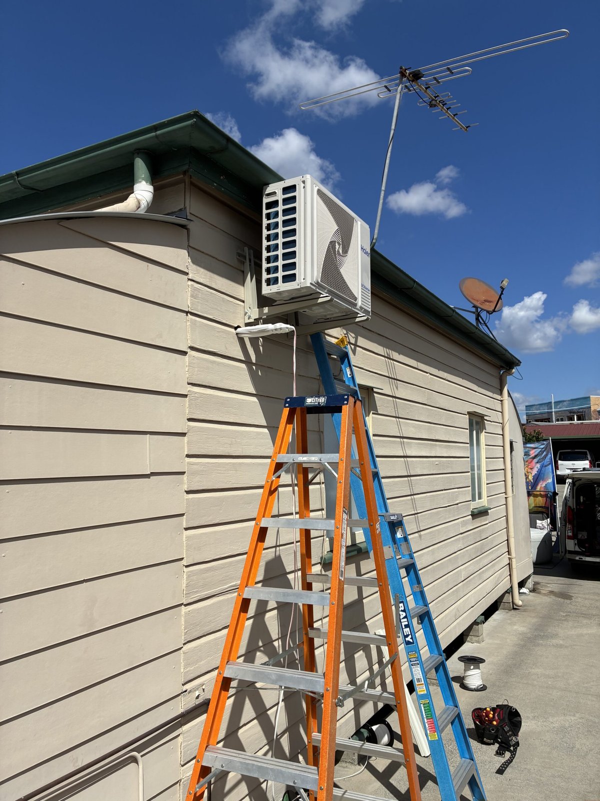 Haier split system outdoor unit installation in progress at Alexandra Hills home — ladders and Amplus van on site
