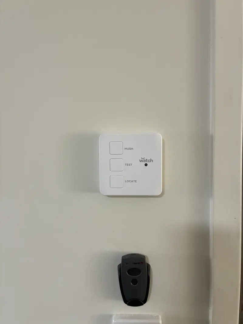 Wall-mounted smoke alarm control panel with hush, test and locate buttons plus wireless remote