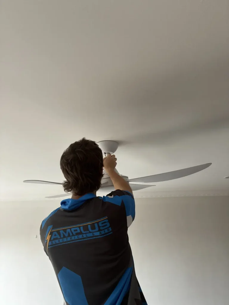 Amplus Electrical & Air electrician installing a ceiling fan in a Redlands home, Amplus logo on shirt