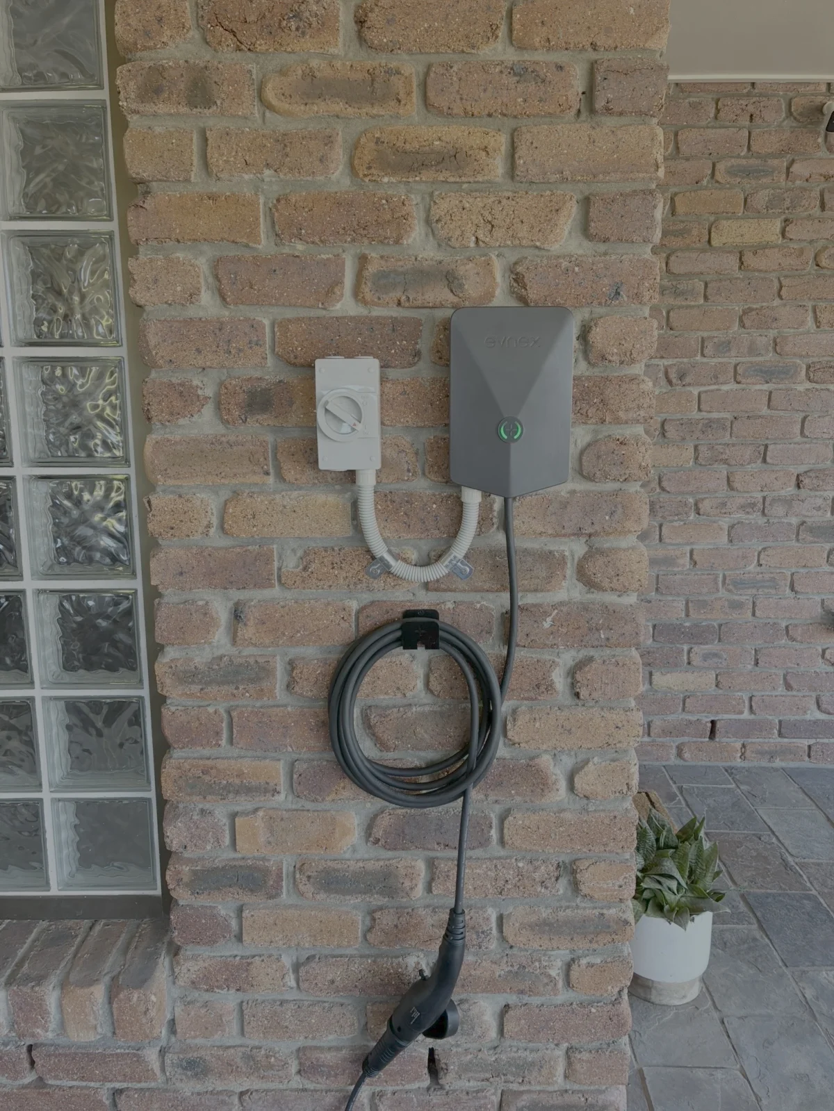 Close-up of an Evnex EV charger mounted on a brick wall in Brisbane